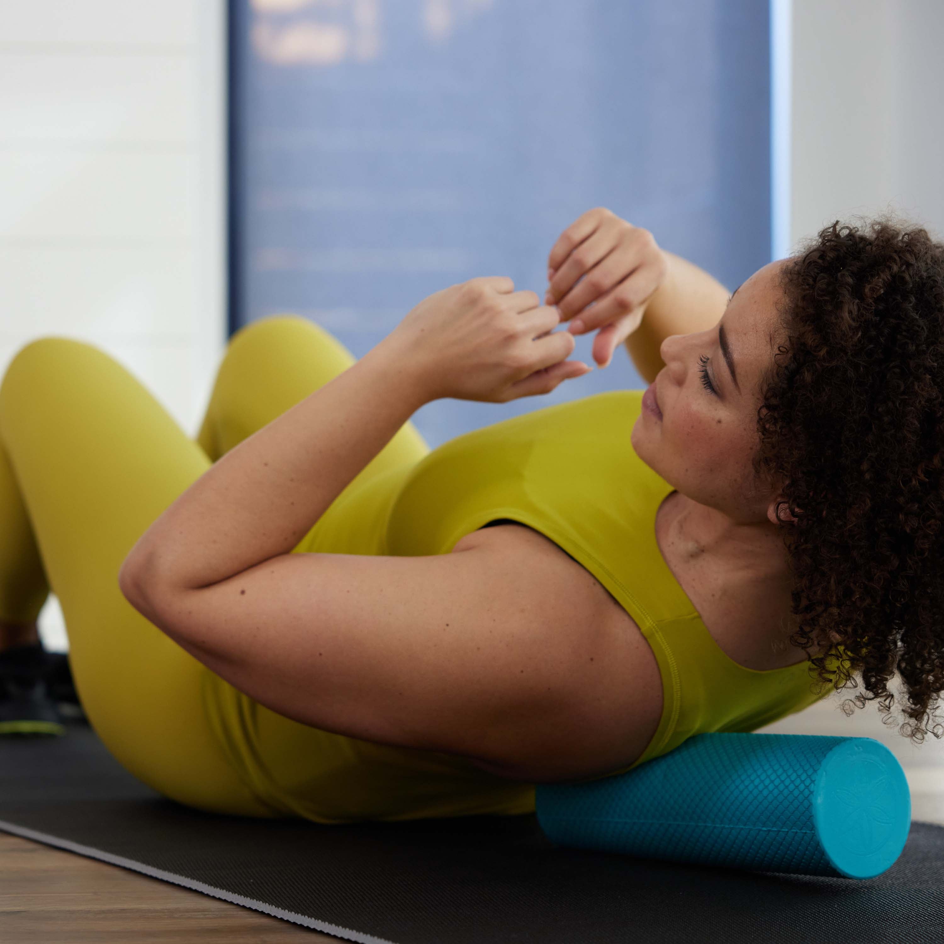Person on laying in yoga mat with the Restore Compact Foam Roller under the shoulder blade massaging